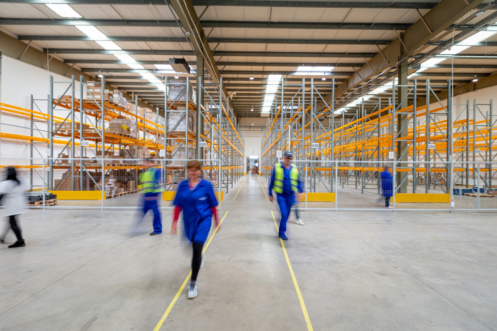 Workers walking through the aisles of a large, brightly lit warehouse
